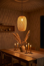 Hana Cocoon bamboo pendant light glowing at night above a candlelit oak dining table