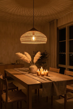 Panier Saucer rattan pendant light glowing at night above a candlelit dining table